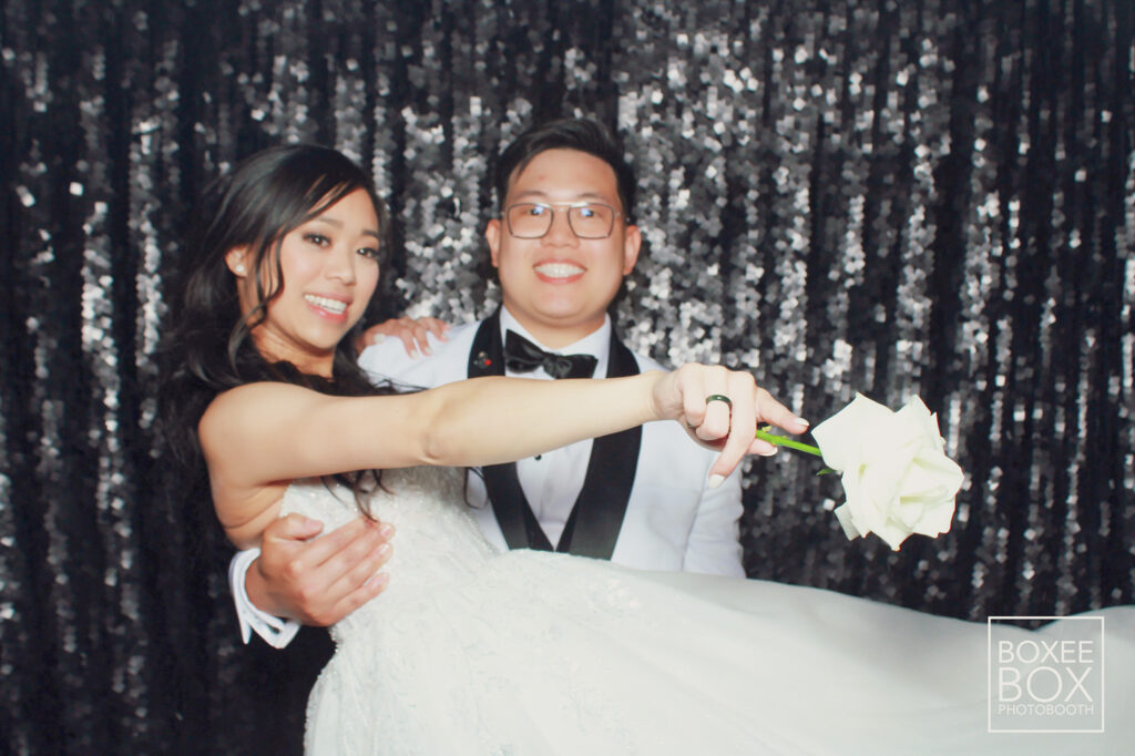 groom picks up bride holding white rose in photo booth houston
